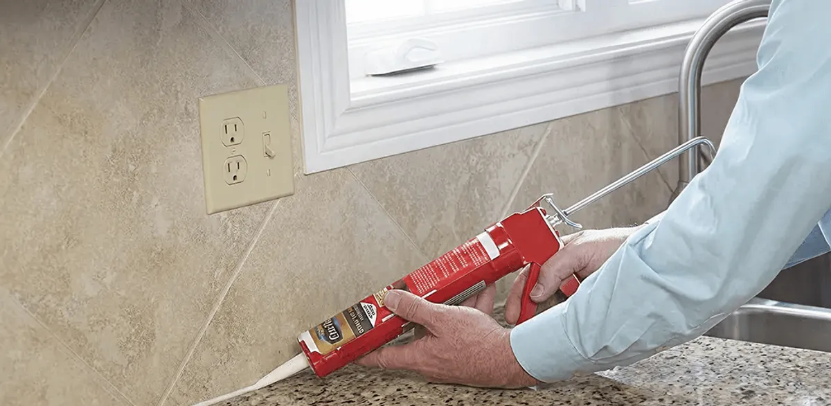 Handyman applying caulk along a kitchen backsplash and countertop seam in Dayton, OH