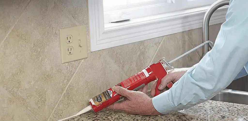 Handyman applying caulk along a kitchen backsplash and countertop seam in Dayton, OH